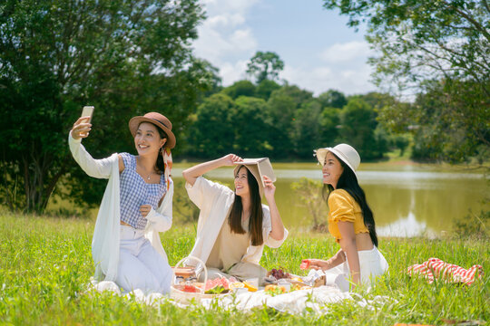 Asian woman friends, they are having picnic, eating in the morning, They are taking pictures to check in.