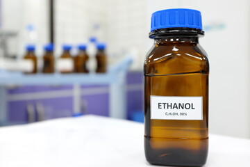 Selective focus of ethanol or ethyl alcohol brown amber glass bottle inside a laboratory. Blurred background with copy space. - obrazy, fototapety, plakaty