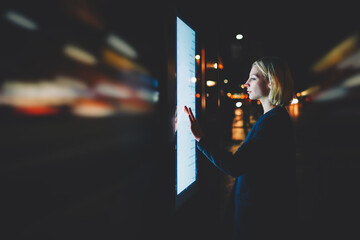 Motion blur effect, female using automated teller machine with big digital screen while standing in night city out-of-focus lights,woman verifies account balance on banking application modern device