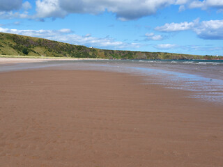 sandy beach on low tide, green hills visible at the distance