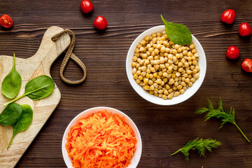 Vegetarian meal. Chickpeas and carrot in bowls on dark wooden table top view