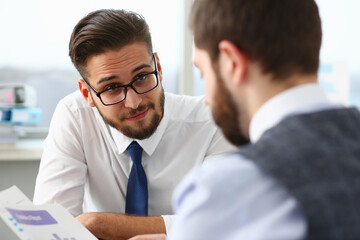 Smiling male in classic tie and glasses is talking with colleague who is holding financial chart