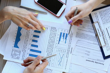 Top view close up of male and two females hands as they are sitting at desk with documents and holding pens