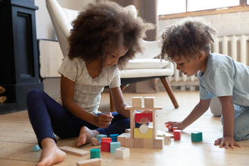 Playful little biracial kids siblings sit on warm floor at home build play with wooden bricks together, small african American brother and sister children construct with blocks cubes in living room - Powered by Adobe