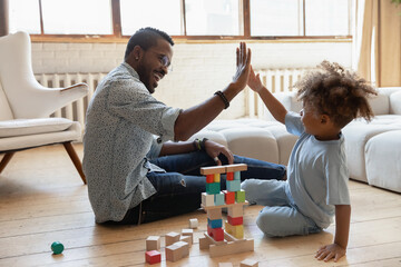 Happy young african American father and little ethnic son give high five playing together with...