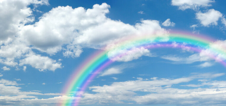 Sunny summer blue sky panoramic rainbow - big fluffy clouds with a giant arcing rainbow against a beautiful summertime blue sky with copy space for messages

