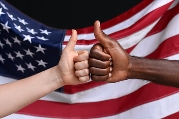 Hands of Caucasian woman and African-American man showing thumb-up gesture near national flag of...