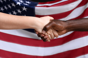 Caucasian woman and African-American man shaking hands near national flag of USA. Racism concept