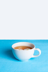 A minimalistic composition of one white cup of chamomile tea on a white-blue background. Place for text.