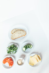 Top view of ingredients for a healthy sandwich, on a white surface. Slices of bread, cucumber, lettuce, cheese and tomato.