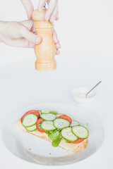 Healthy sandwich with two hands holding a pepper mill above it