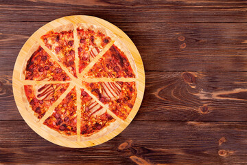 Sliced BBQ pizza with ham, bbq sauce, bacon and salami on a round wood platter which is on wooden rustic background, top view and copy space