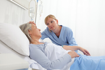 Fototapeta premium nurse take comfort elderly woman lying in the hospital room bed, by stroking her and holding the arm where the drip needle is, concept of loneliness and old age diseases