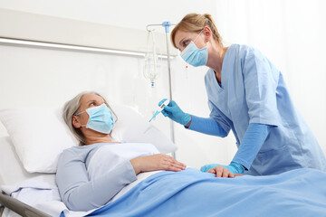 Fototapeta na wymiar nurse with thermometer measures fever on elderly woman patient lying in the hospital room bed, wearing protective gloves and medical surgical mask, coronavirus covid 19 protection concept