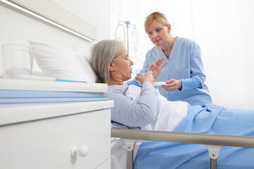 nurse gives the pill to the elderly woman patient lying in the hospital room bed, concept of...