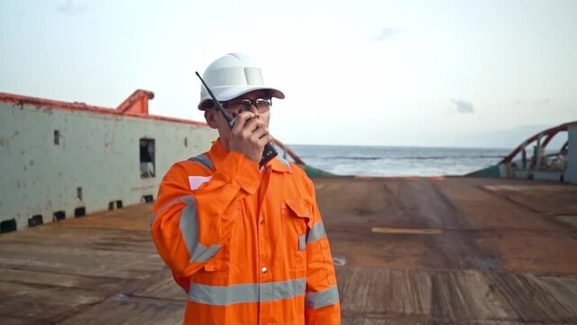 Filipino deck Officer on deck of vessel or ship , wearing PPE personal protective equipment. He speaks to VHF walkie-talkie radio in hands. Dream work at sea
