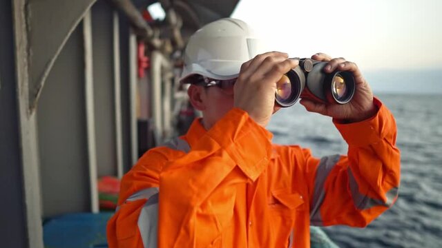 Filipino deck Officer on deck of vessel or ship , wearing PPE personal protective equipment. He is looking through binoculars.