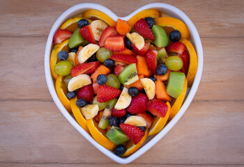 Fresh fruit salad in a white ceramic plate heart shaped. Wooden background