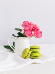 Three tasty French macarons and a jar with beautiful roses on a white background. Place for text.