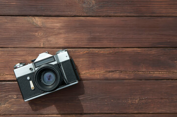 an old retro film camera with scratches dust and a black lens on a wooden table made of planks with copy space  in the lower left corner of the image