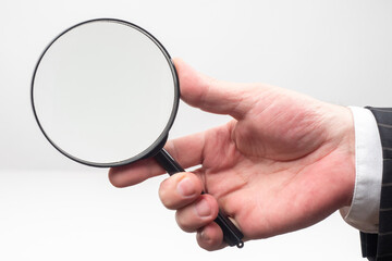 Magnifying glass in a man hand. Human holds a magnifier. Magnifying glass on a light background. Concept - a person is considering something. Concept - selling lenses to enlarge.