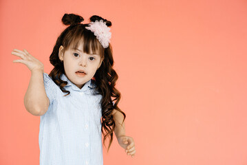 Surprised girl with Down syndrome in a dress, pink background in the background. Happy baby...