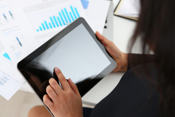 Top view cropped head close up of female studying financial documents and typing on digital tablet