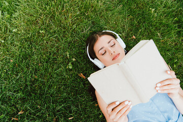 top view of attractive woman in wireless headphones lying on grass and reading book