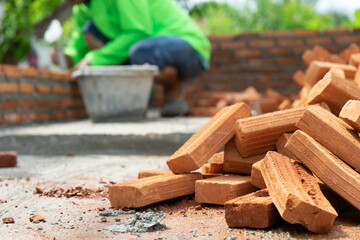 Closeup bulk of red brick at the construction site with blurred worker working in background