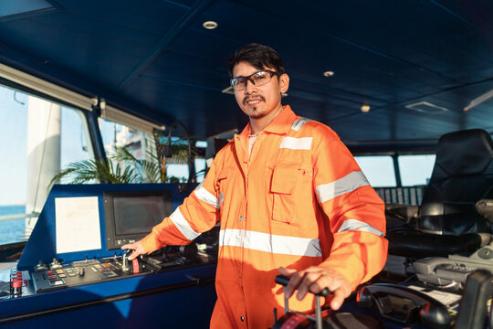 Filipino deck Officer on bridge of vessel or ship wearing coverall during navigaton watch at sea . He is maneuvering with cpp thrusters propulsion