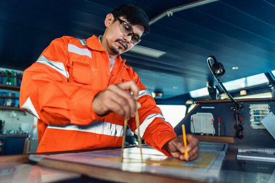 Filipino deck Officer on bridge of vessel or ship wearing coverall during navigaton watch at sea . He is plotting position on chart