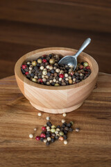Wooden bowl with pepper kernels and a spoon on a wooden surface
