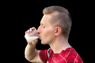 The guy drinks milk on a black background. Organic milk in the guy's hand. Handsome young man