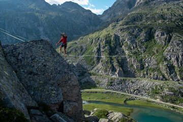 Lago Nero, Pinzolo, Italy - 2020 july 18th: young boy with red hoodie and hat practising slackline on a rope hanging between two peaks