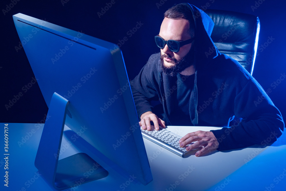 Poster hacker in a hood on a dark background. harker face illuminates light of a computer. male hacker and 