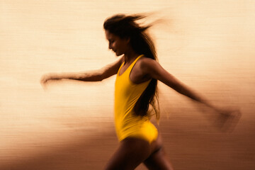 Artistic speed blur of young woman running against yellow wall
