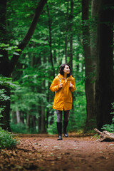 woman in yellow raincoat walking by rainy forest