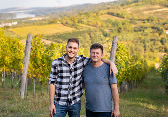 Father and son, standing together in vineyard. Small family business.
