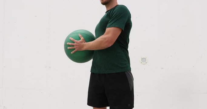 Medicine ball exercises - man doing standing rotation side to side aka standing russian twist. Fit male athlete showing strength training exercises using medicine ball.