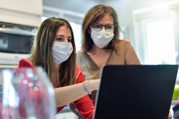 Two female colleagues  wearing a protective mask while they are  attending at a  meeting on a video call on their computer during the lockdown due to the coronavirus