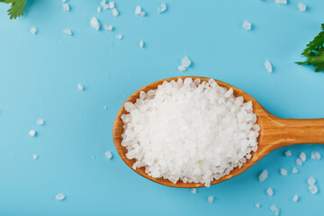 Sea salt in a wooden spoon on Large salt crystals with greens on a blue background.