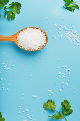 Sea salt in a wooden spoon on Large salt crystals with greens on a blue background.