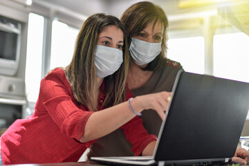 Mother and daughter wearing protective mask and browsing and shopping on the web at home on their computer during lockdown due to covid-19