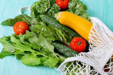 Vegetable and greenery assortment in mesh bag against the green background. Kale, chard, arugula, zucchini, cucumber and tomato. Zero waste shopping
