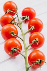 Beautiful fresh cherry tomatoes on a twig on a white wooden background close-up. Healthy wholesome food.