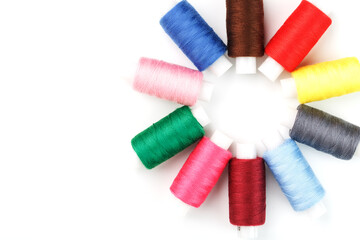 Sewing threads of different colors on reels on a white background in a circle.