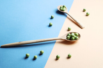 Green peas in wooden spoons and scattered peas on a blue-yellow background-the concept of protein nutrition