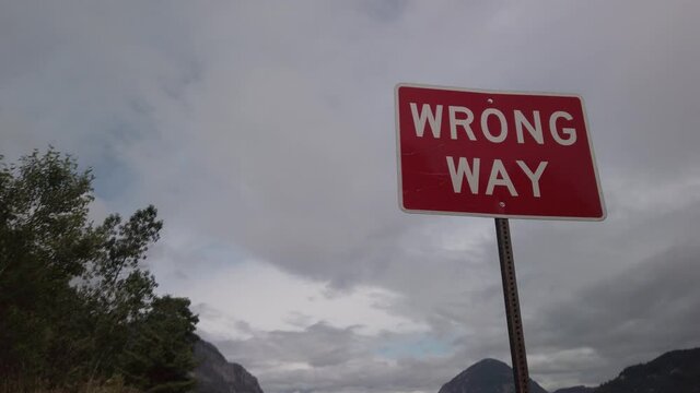 A Wrong Way sign warning of oncoming highway traffic, along a river running through mountains, tilt up and dolly in