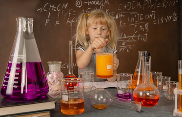 Curious little girl with test tube and colorful orange substance makes tests at school laboratory. Small kid observes chemical reaction. Biology education concept.