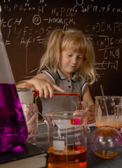 Curious little blonde girl with test tubes pouring orange colorful liquid into laboratory glass. Small kid observes chemical reaction. Biology education concept.